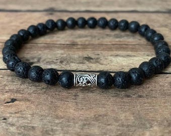 May include: A black lava rock beaded bracelet with a silver charm. The bracelet is made of small, round beads and has a single silver charm in the center.