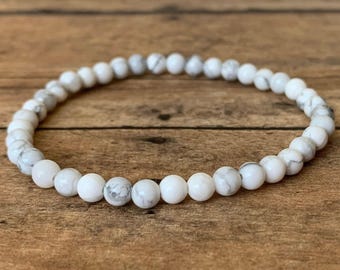 May include: A white howlite beaded bracelet with a simple design. The beads are small and round, and the bracelet is made with a stretchy cord.