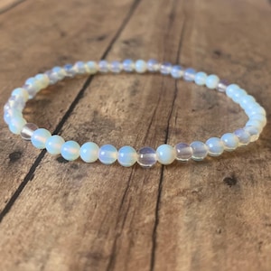 May include: A delicate bracelet made with small, white opal beads. The bracelet is strung on clear elastic and is approximately 7 inches in length.