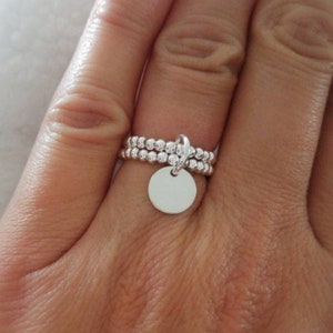 May include: A silver ring with a small, round charm hanging from it. The ring is made of small, round beads.