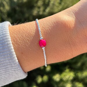Könnte beinhalten: Ein silbernes Perlenarmband mit einer einzigen, leuchtend pinkfarbenen Edelsteinperle.