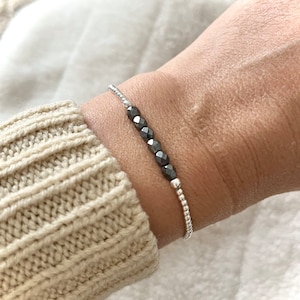 Peut inclure: Un bracelet argenté avec une rangée de perles gris foncé.