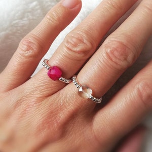 Può includere: Due anelli d'argento con bande di perline e accenti di pietre preziose sfaccettate. Un anello presenta una pietra preziosa rosa e l'altro una pietra preziosa trasparente.