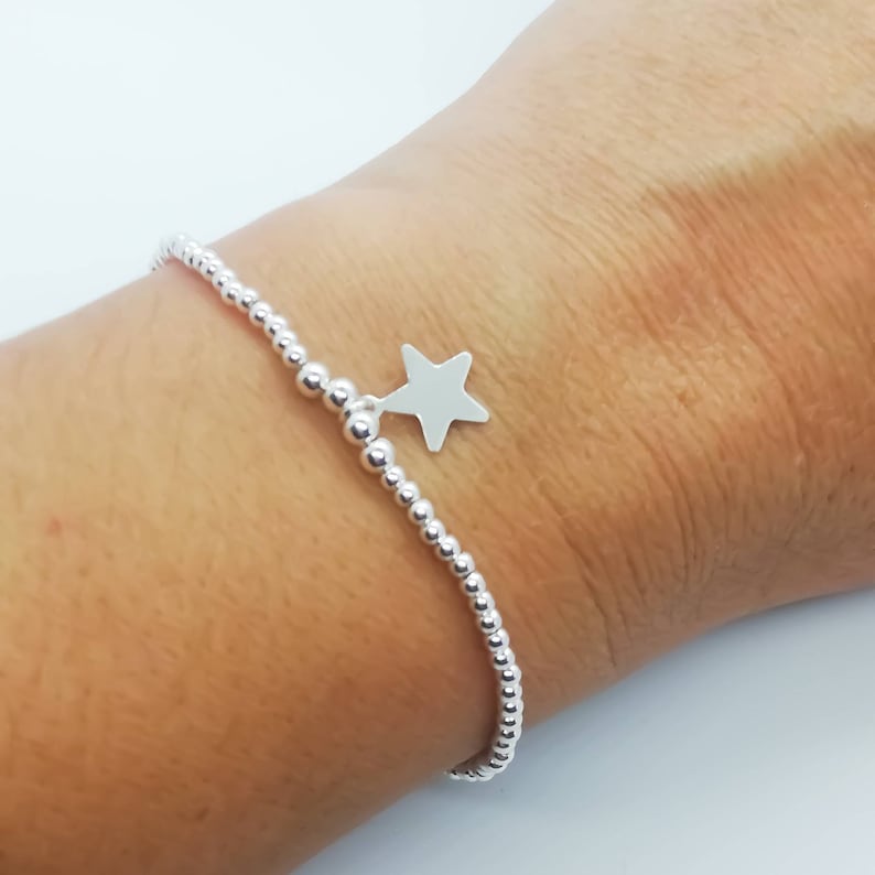 May include: A silver beaded bracelet with a star charm. The bracelet is on a person's wrist.
