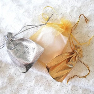 May include: Three small drawstring bags, one silver, one gold, and one white with a sheer, gauzy texture.