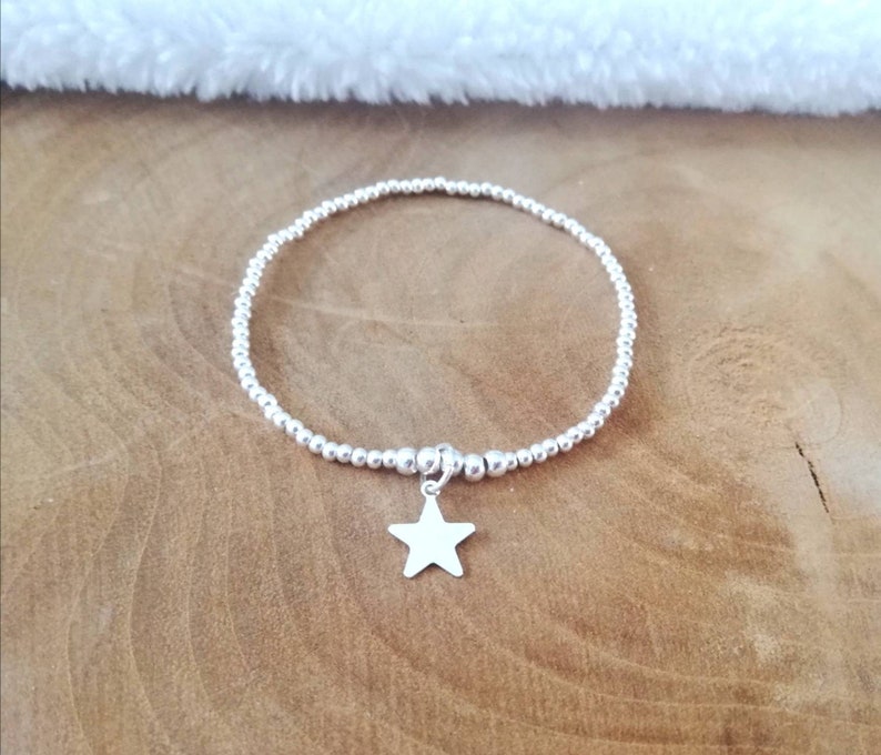 May include: A silver beaded bracelet with a star charm. The bracelet is made of small, round beads and has a simple, elegant design.