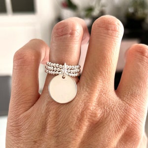 Puede incluir: Un anillo de plata con un dije redondo. El anillo está hecho de múltiples bandas de pequeñas cuentas.
