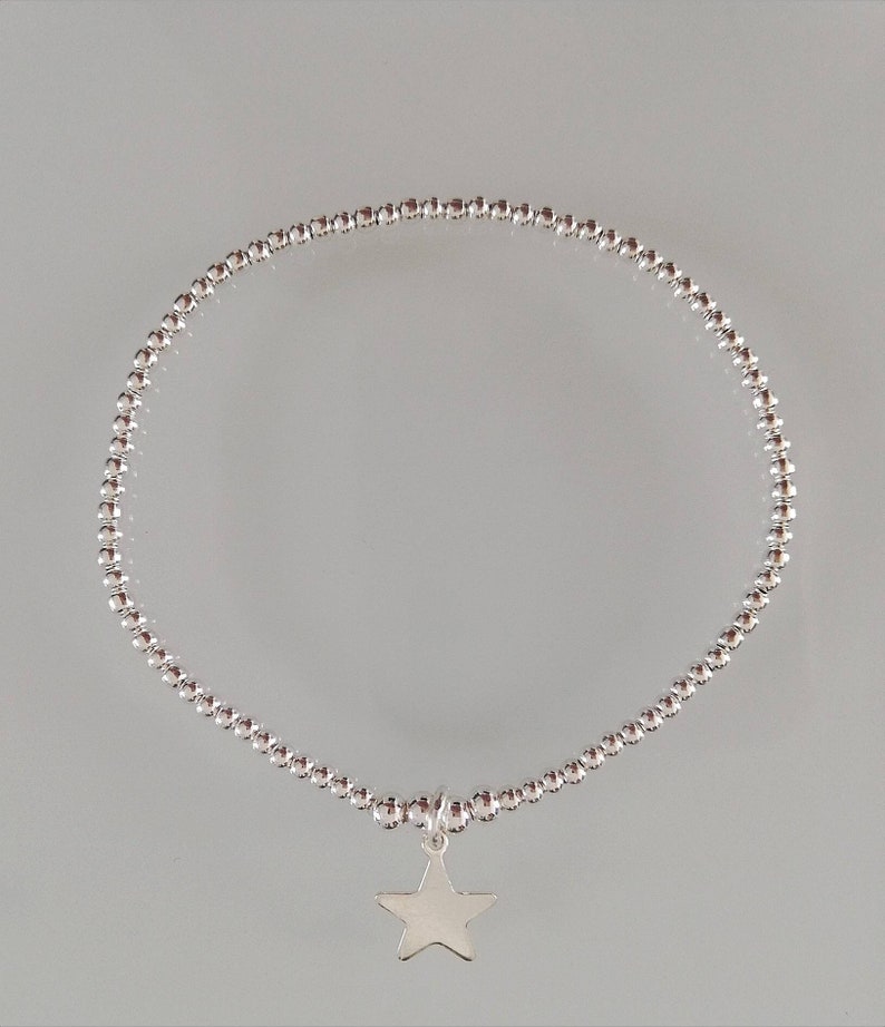 May include: A silver beaded bracelet with a star charm. The bracelet is made of small, round beads and has a simple, elegant design.