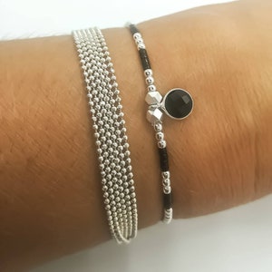 Peut inclure: Deux bracelets sur un poignet. Un bracelet est une chaîne argentée à plusieurs brins. L'autre bracelet est noir et argent avec un charme en pierre précieuse noire.