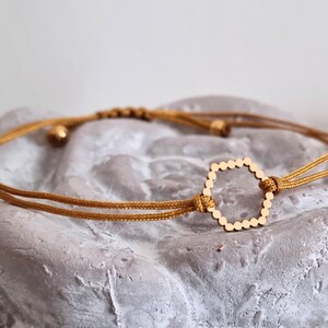 May include: A gold-toned hexagonal charm bracelet with a brown cord. The bracelet is adjustable and can be worn on the wrist or ankle.