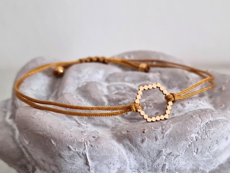 May include: A gold-toned hexagonal charm bracelet with a brown cord. The bracelet is adjustable and can be worn on the wrist or ankle.