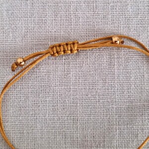 May include: A gold cord bracelet with two small gold beads. The cord is knotted in a decorative pattern.