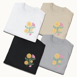 May include: Four folded t-shirts in white, beige, black, and gray with a floral design and the text "The Trust Process" printed on the front.