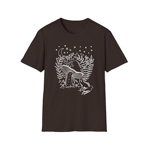 May include: A dark brown t-shirt with a white outline of a mushroom, leaves, and a frog in a forest setting. The design includes a crescent moon and stars.