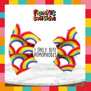 May include: A hair bow featuring a repeating rainbow pattern in red, orange, yellow, green, blue, and purple. A circular white center piece displays the black text I ONLY BITE HOMOPHOBES. The brand name FRANKY'S BOWTIQUE appears above the bow.