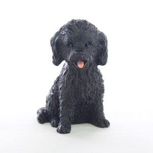 May include: Black figurine of a small dog with curly fur, sitting with its tongue sticking out.