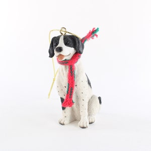 May include: A black and white dog figurine wearing a red and green scarf. The figurine is a Christmas ornament.