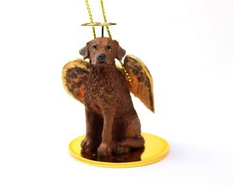 May include: A brown and white dog figurine with angel wings, wearing a gold halo, sitting on a gold base. The figurine is a Christmas ornament.