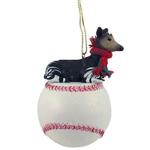 May include: A white baseball ornament with red stitching and a black and white okapi figurine wearing a red and green scarf sitting on top.