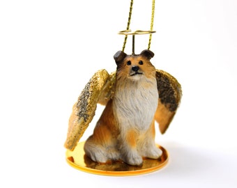Könnte beinhalten: Eine kleine, braune und weiße Hundefigur mit goldenen Flügeln und einem Heiligenschein. Die Figur sitzt auf einem goldenen Sockel und ist zum Aufhängen als Ornament gedacht.