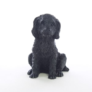 May include: Black ceramic figurine of a sitting dog. The dog has a curly coat and is looking directly at the camera.