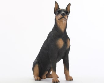 May include: A black and brown figurine of a Doberman Pinscher dog sitting with its head tilted up.