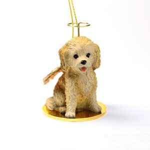 May include: A small, cream-colored dog figurine with angel wings and a halo. The figurine is sitting on a gold base and is ready to hang as an ornament.