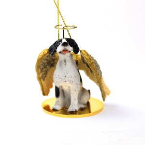 May include: A black and white dog with a gold halo and wings. The dog is sitting on a gold base. The ornament is made of resin and is a memorial ornament for a pet.
