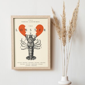 May include: Framed movie poster for "The Lobster" film. The poster features a detailed illustration of a lobster with two orange heart shapes above it. The film title and director's name are displayed in a minimalist font.