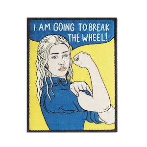 Può includere: Una toppa ricamata gialla e blu con una donna con lunghi capelli bianchi che flette il bicipite. Il testo sulla toppa recita "I am going to break the wheel!"