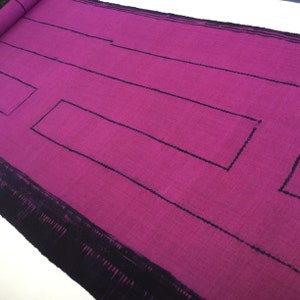 May include: A close-up of a pink fabric with black lines forming geometric shapes. The fabric has a textured surface.