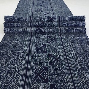 Könnte beinhalten: Ein blauer und weißer Indigo-Stoff mit einem geometrischen Muster. Der Stoff ist in mehreren Schichten gefaltet, wodurch das Muster auf beiden Seiten sichtbar wird.