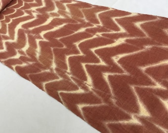 Peut inclure: Un long morceau de tissu avec un motif chevron brun et blanc. Le tissu est plié et roulé à une extrémité.