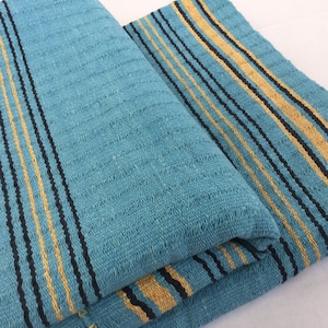 May include: A folded blue and yellow striped throw blanket with black stripes. The blanket is made of a soft, textured fabric.