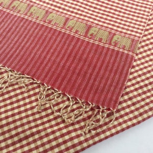 May include: Red and cream checkered fabric with a red and cream striped fabric with a fringe edge. The striped fabric has a pattern of small elephants.