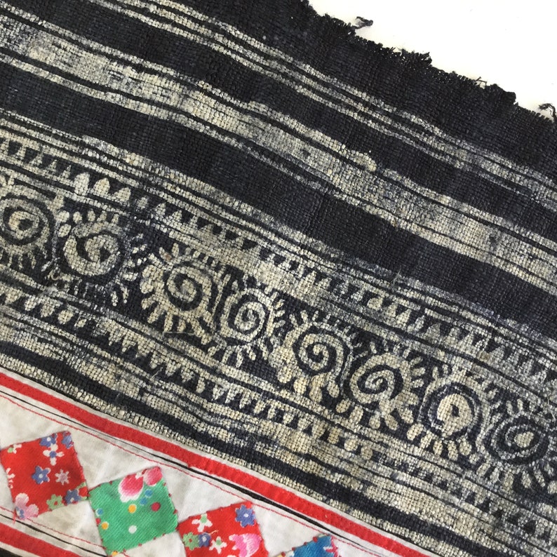 May include: Close-up of a textile with a black and white striped pattern, a decorative border with spiral and floral motifs, and a patchwork section with red, green, and blue floral squares.
