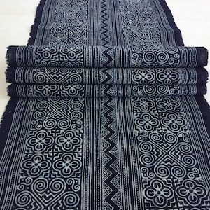Puede incluir: Tela azul índigo con un patrón geométrico blanco. La tela está doblada en tres partes y tiene un borde sin rematar.