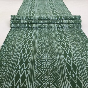Könnte beinhalten: Grüner Stoff mit einem weißen geometrischen Muster. Der Stoff ist dreifach gefaltet und hat eine leicht strukturierte Oberfläche.