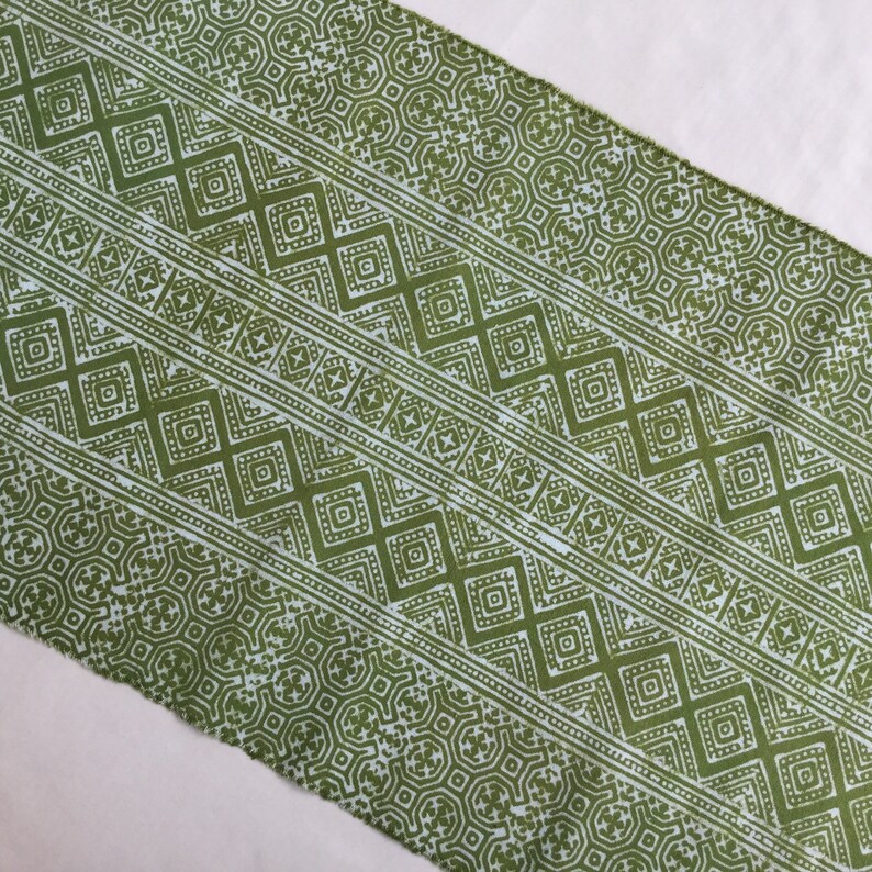Pu&ograve; includere: Tessuto verde con un motivo geometrico bianco. Il motivo &egrave; composto da quadrati, rombi e altre forme.