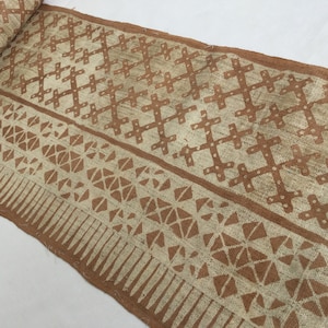 May include: A close-up of a woven fabric with a brown and white geometric pattern. The fabric has a rough texture and is made of natural fibers.