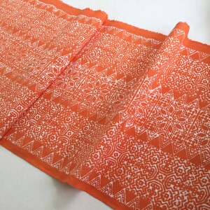 Könnte beinhalten: Orangener Stoff mit einem weißen geometrischen Muster. Das Muster zeigt sich in sich wiederholenden Dreiecken und Rauten.