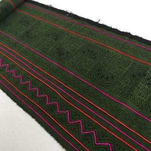 Könnte beinhalten: Grüner Stoff mit einem schwarz-weißen geometrischen Muster und rosa und roten Streifen. Der Stoff hat eine rohe Kante.