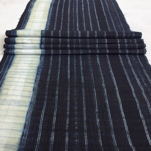 May include: A dark blue and white striped fabric with a white border. The fabric is folded and has a textured surface.