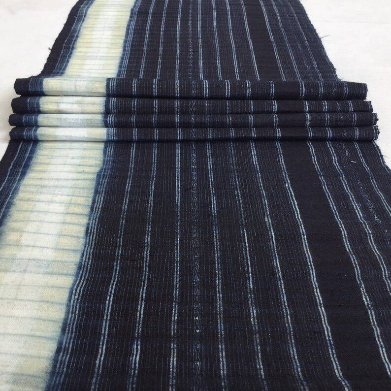 May include: A dark blue and white striped fabric with a white border. The fabric is folded and has a textured surface.