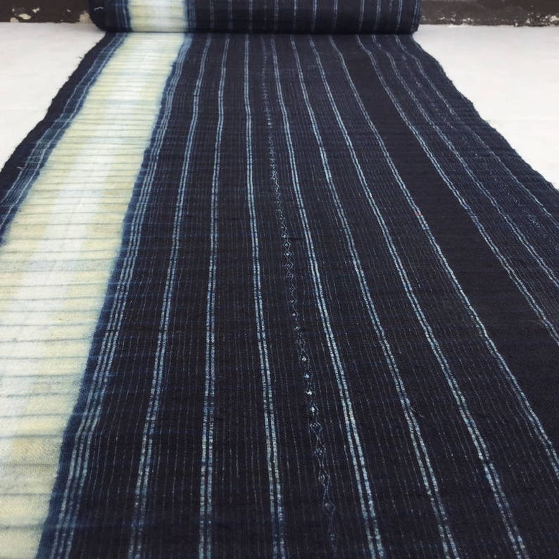 May include: A close-up of a blue and white striped fabric. The fabric has a textured surface and is woven with thin stripes. The fabric is folded in half and the stripes are running vertically.