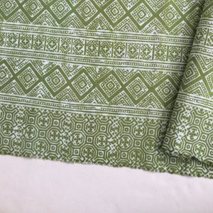 Pu&ograve; includere: Tessuto verde con un motivo geometrico bianco. Il tessuto ha un bordo sfrangiato.