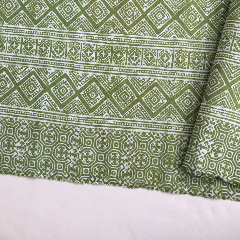 Pu&ograve; includere: Tessuto verde con un motivo geometrico bianco. Il tessuto ha un bordo sfrangiato.