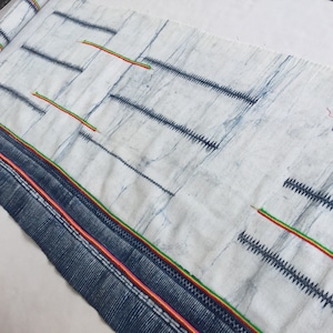 May include: A white fabric with a blue and white pattern. The fabric has a green, yellow, and pink border.