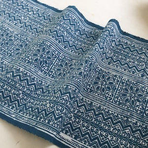 Könnte beinhalten: Blauer und weißer Stoff mit einem sich wiederholenden geometrischen Muster. Der Stoff hat eine strukturierte Oberfläche und ist in der Mitte gefaltet.