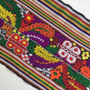 May include: A black fabric with colorful embroidered butterflies and floral designs. The fabric has a striped pattern in shades of red, green, yellow, and white.